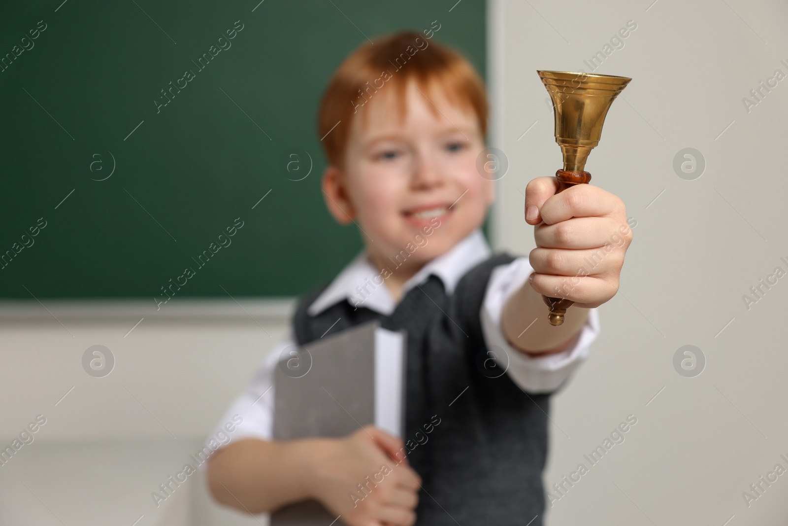 Photo of Cute little boy ringing school bell in classroom, focus on hand