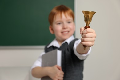 Photo of Cute little boy ringing school bell in classroom, focus on hand