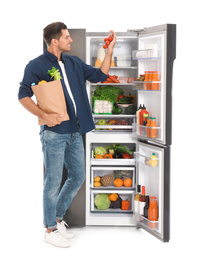 Photo of Man with bag of groceries and tomatoes near open refrigerator on white background
