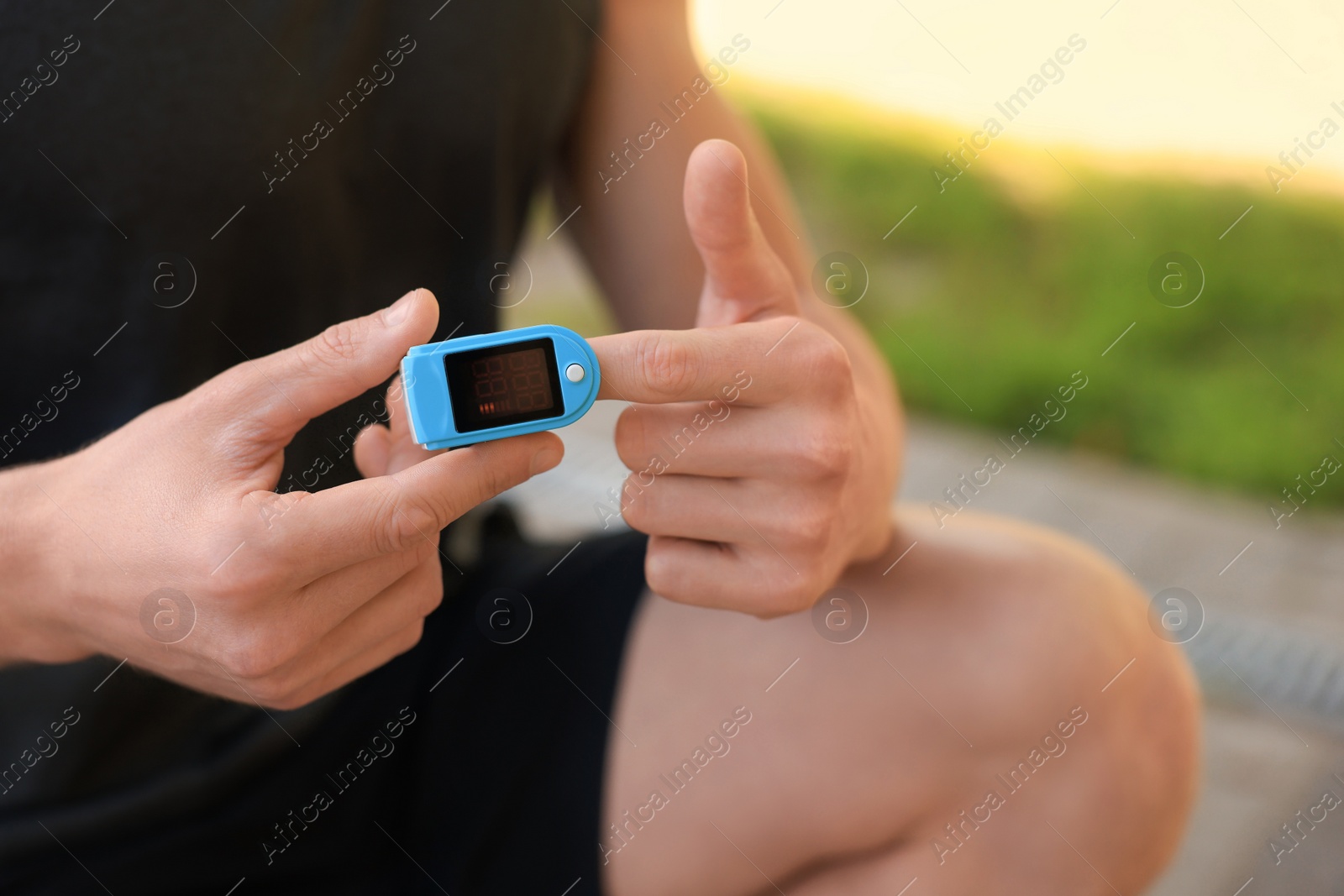 Photo of Man checking pulse with blood pressure monitor on finger after training outdoors, closeup