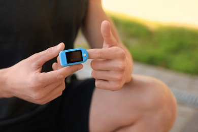 Photo of Man checking pulse with blood pressure monitor on finger after training outdoors, closeup
