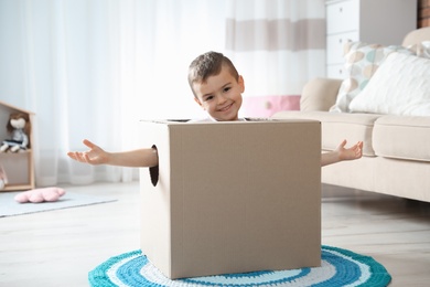 Photo of Cute little boy playing cardboard box in living room