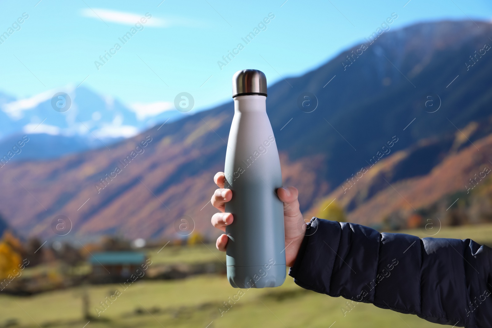 Photo of Boy holding thermo bottle with drink in mountains on sunny day, closeup