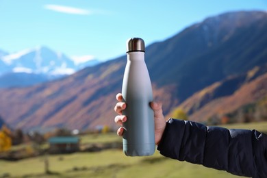 Boy holding thermo bottle with drink in mountains on sunny day, closeup