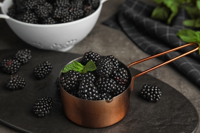 Metal saucepan with tasty blackberries on grey table