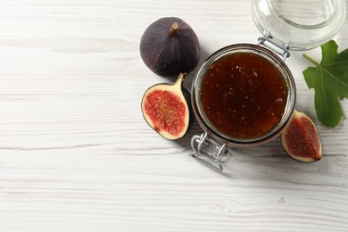 Photo of Glass jar with tasty sweet jam, green leaf and fresh figs on white wooden table, flat lay. Space for text
