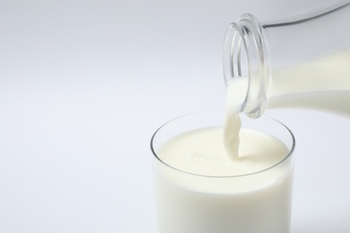 Photo of Pouring milk into glass on white background, closeup