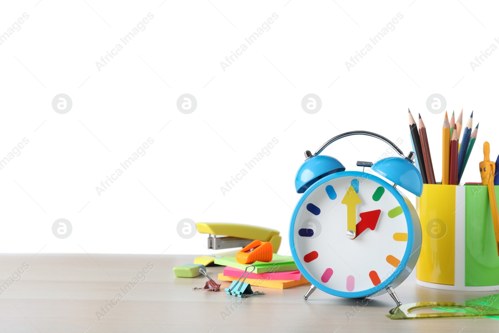 Photo of Light blue alarm clock and different stationery on wooden table against white background, space for text. School time