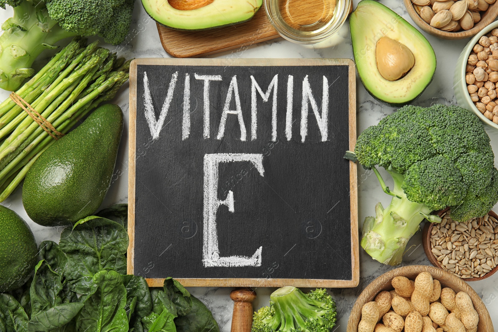 Photo of Small chalkboard with phrase Vitamin E and different products on white marble table, flat lay