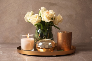 Tray with burning wax candles and flowers on table