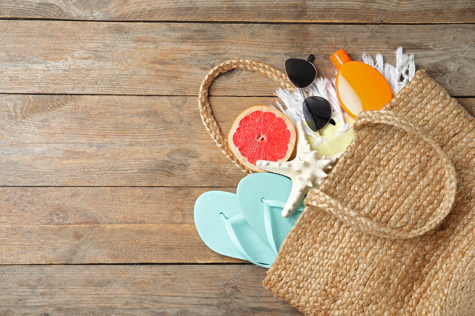 Photo of Beach objects in bag and space for text on wooden background, flat lay