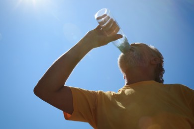 Photo of Senior man drinking water to prevent heat stroke outdoors, low angle view