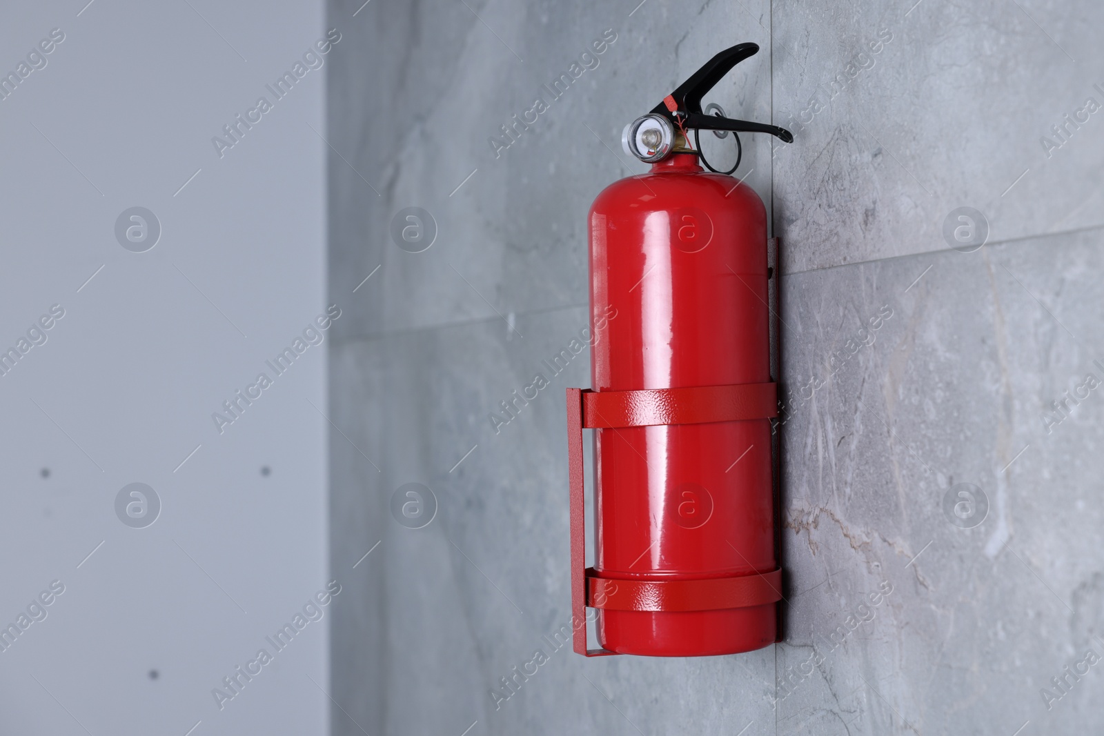 Photo of Fire extinguisher on grey wall, space for text