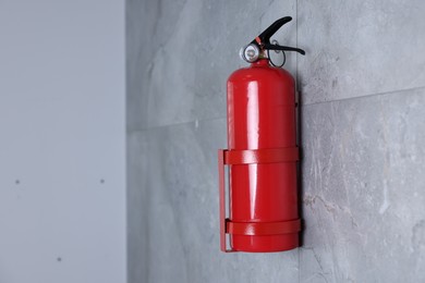 Fire extinguisher on grey wall, space for text