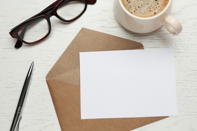 Photo of Envelope with blank paper card, cup of coffee, pen and glasses on white wooden table, flat lay