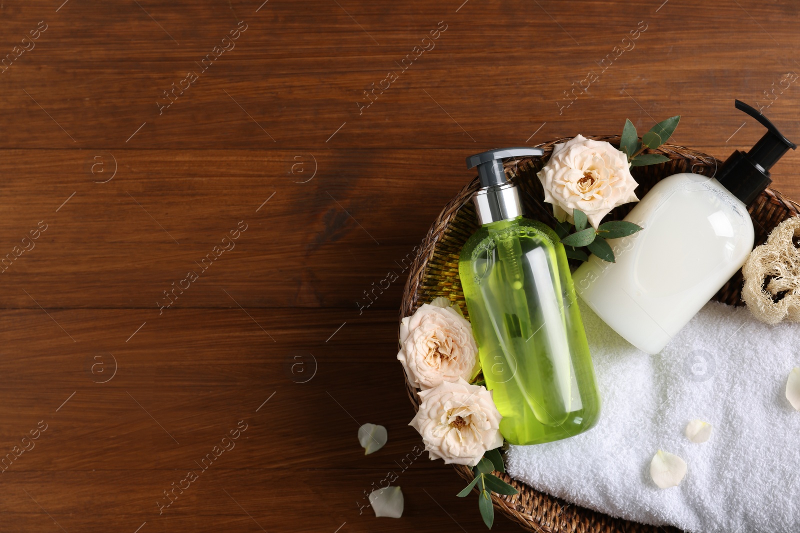 Photo of Dispensers of liquid soap, towel and roses in wicker basket on wooden table, top view. Space for text
