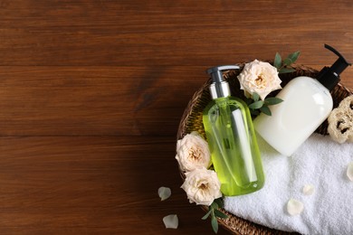 Dispensers of liquid soap, towel and roses in wicker basket on wooden table, top view. Space for text