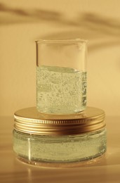 Photo of Jar and glass beaker with cosmetic gel on light background