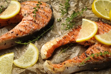 Photo of Tasty grilled salmon steaks, lemon slices and thyme on parchment paper