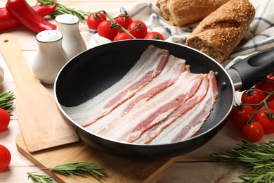 Slices of raw bacon in frying pan and fresh products on wooden table, closeup