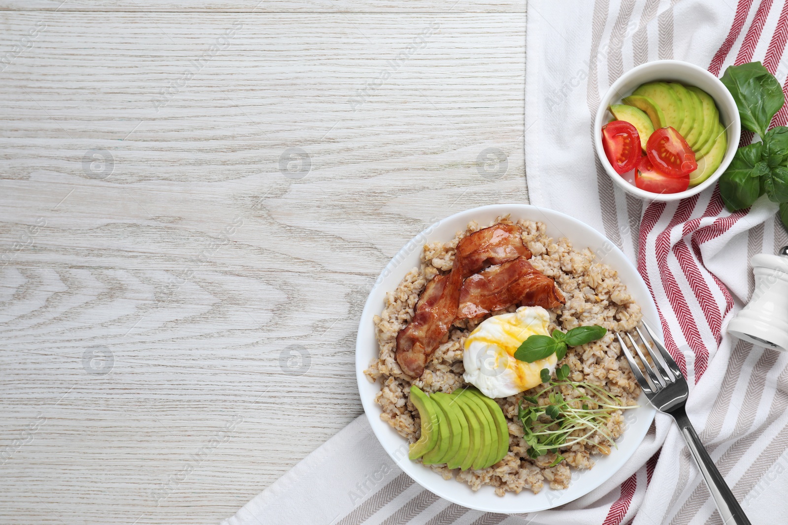 Photo of Delicious boiled oatmeal with poached egg, bacon and avocado served on light wooden table, flat lay. Space for text