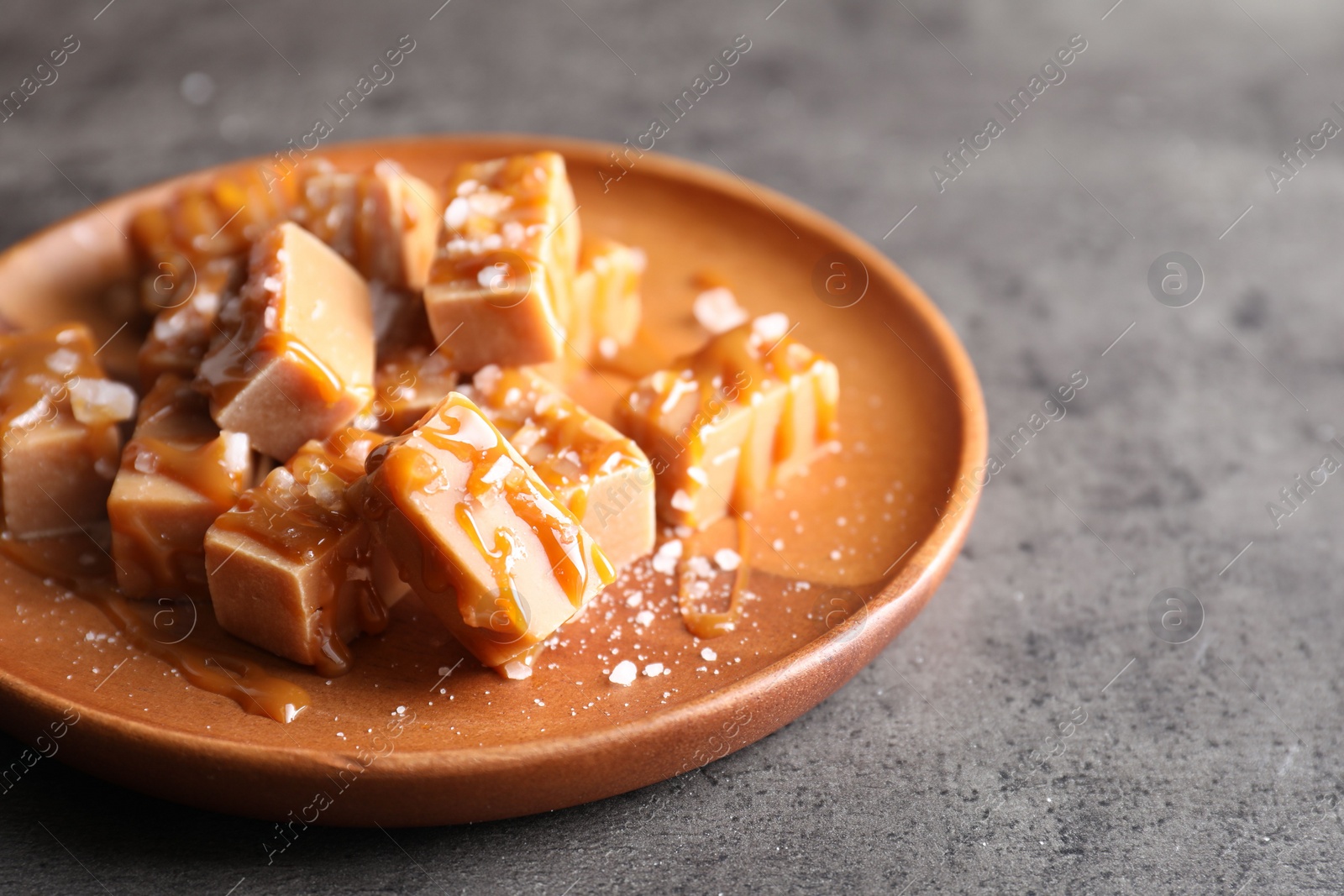 Photo of Plate with tasty candies, caramel sauce and salt on grey table, closeup. Space for text