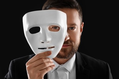 Multiple personality concept. Man covering face with mask on black background