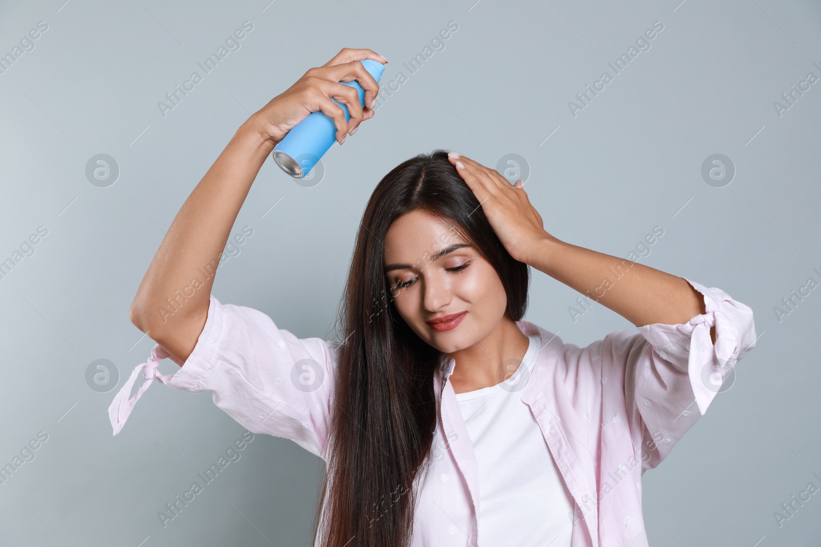 Photo of Woman applying dry shampoo onto her hair on light grey background