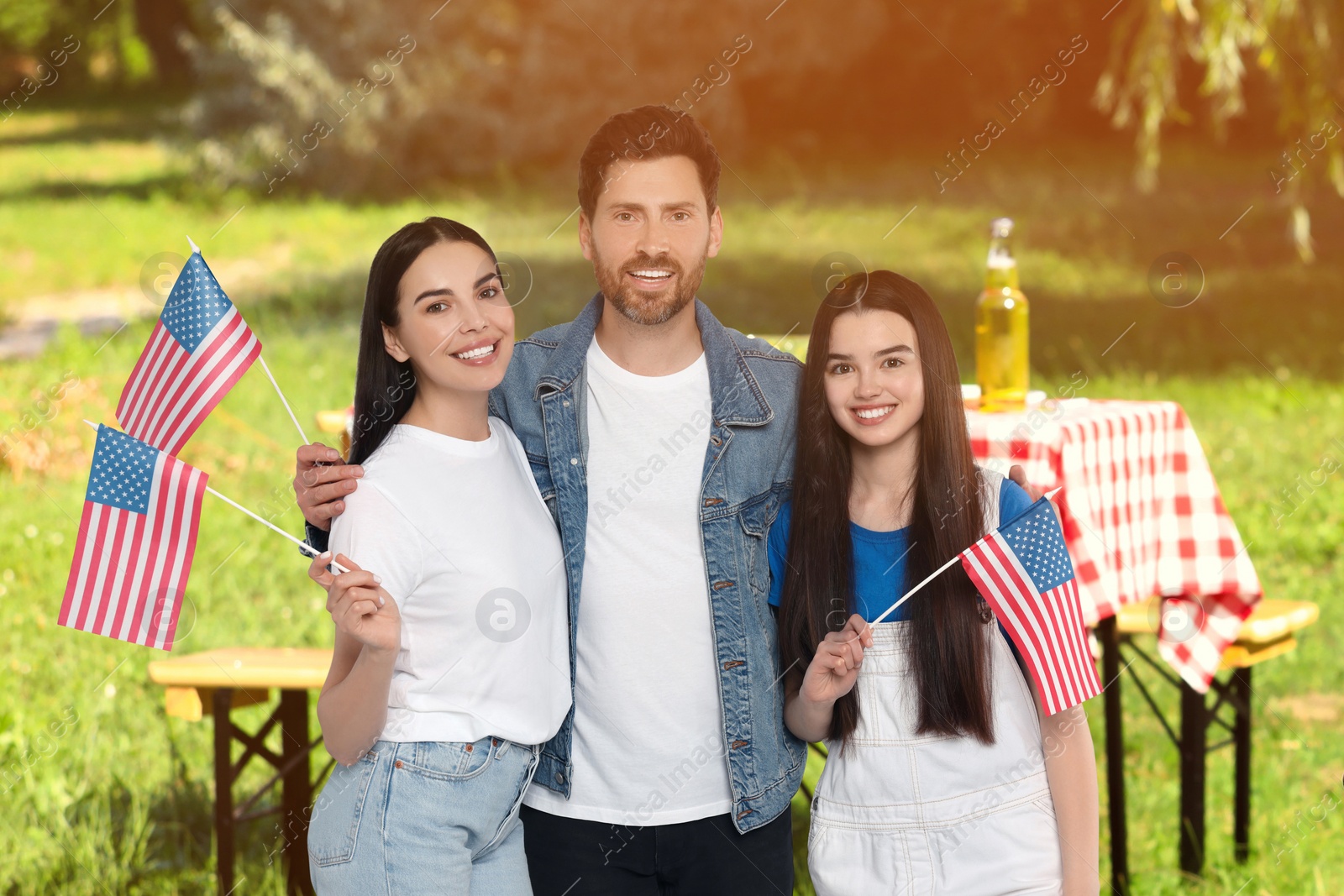 Image of 4th of July - Independence day of America. Happy family with national flags of United States having picnic in park