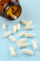 Photo of Bottle and vitamin capsules on light blue background, closeup