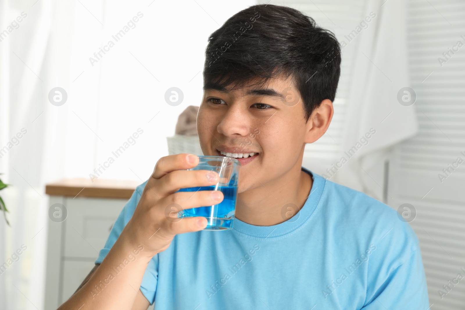 Photo of Man holding glass with mouthwash in bathroom. Teeth care