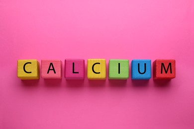 Word Calcium made of colorful wooden cubes with letters on bright pink background, flat lay