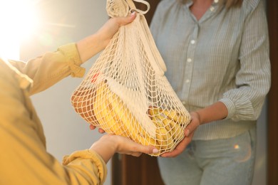 Photo of Young woman with net bag of products helping her senior neighbour outdoors on sunny day, closeup