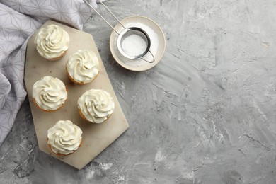 Tasty cupcakes with vanilla cream on grey table, top view. Space for text