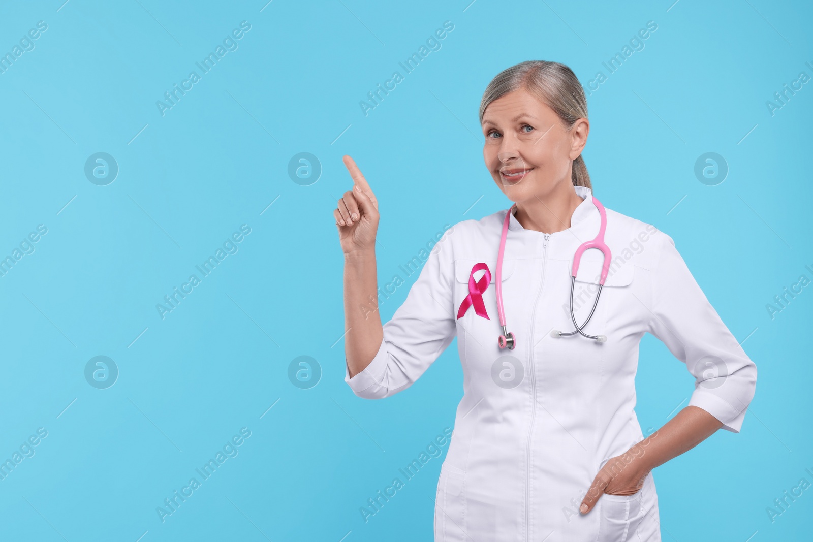 Photo of Doctor with pink ribbon and stethoscope on light blue background, space for text. Breast cancer awareness