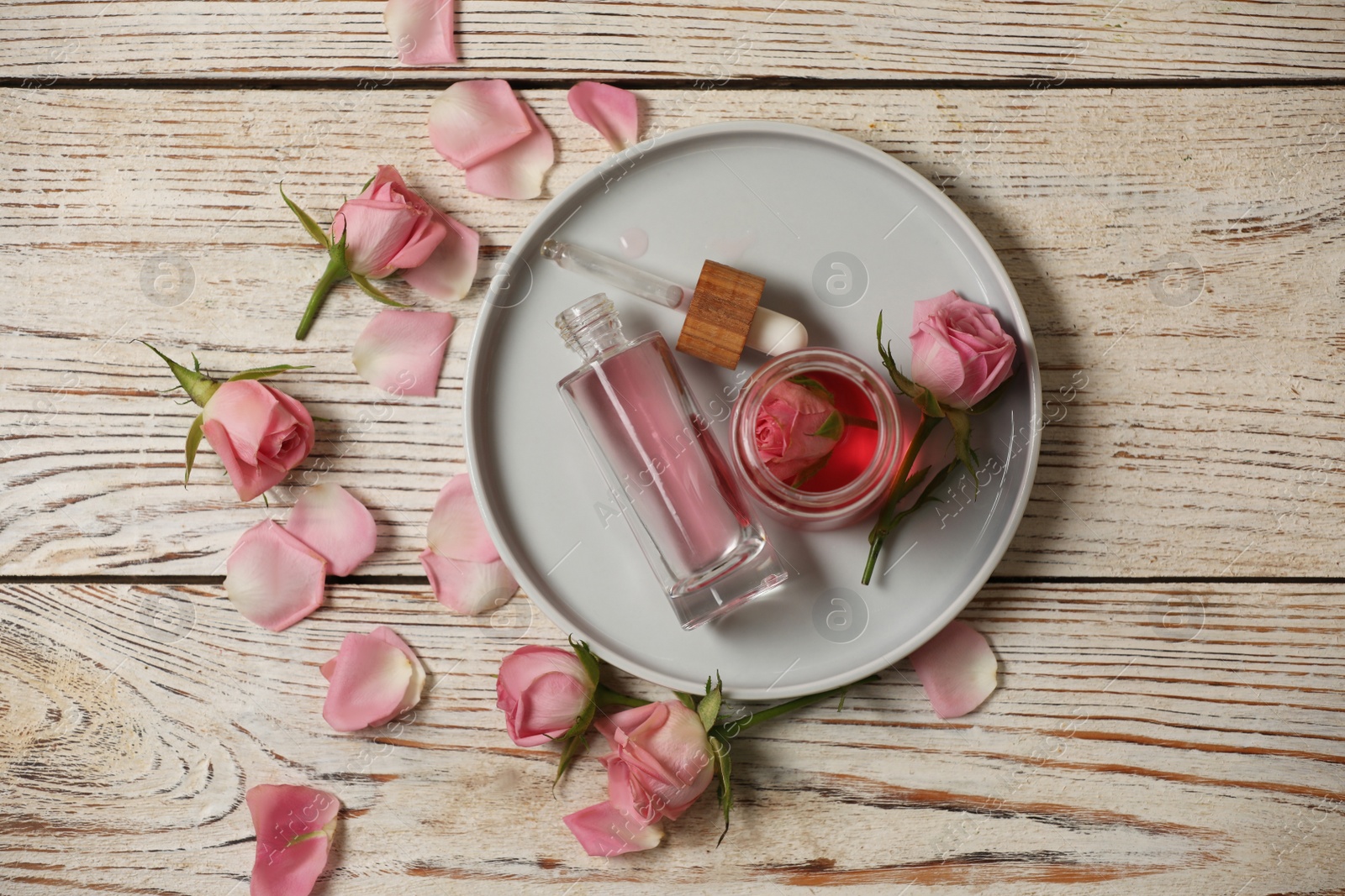 Photo of Flat lay composition with essential rose oil and flowers on white wooden table