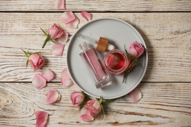 Photo of Flat lay composition with essential rose oil and flowers on white wooden table