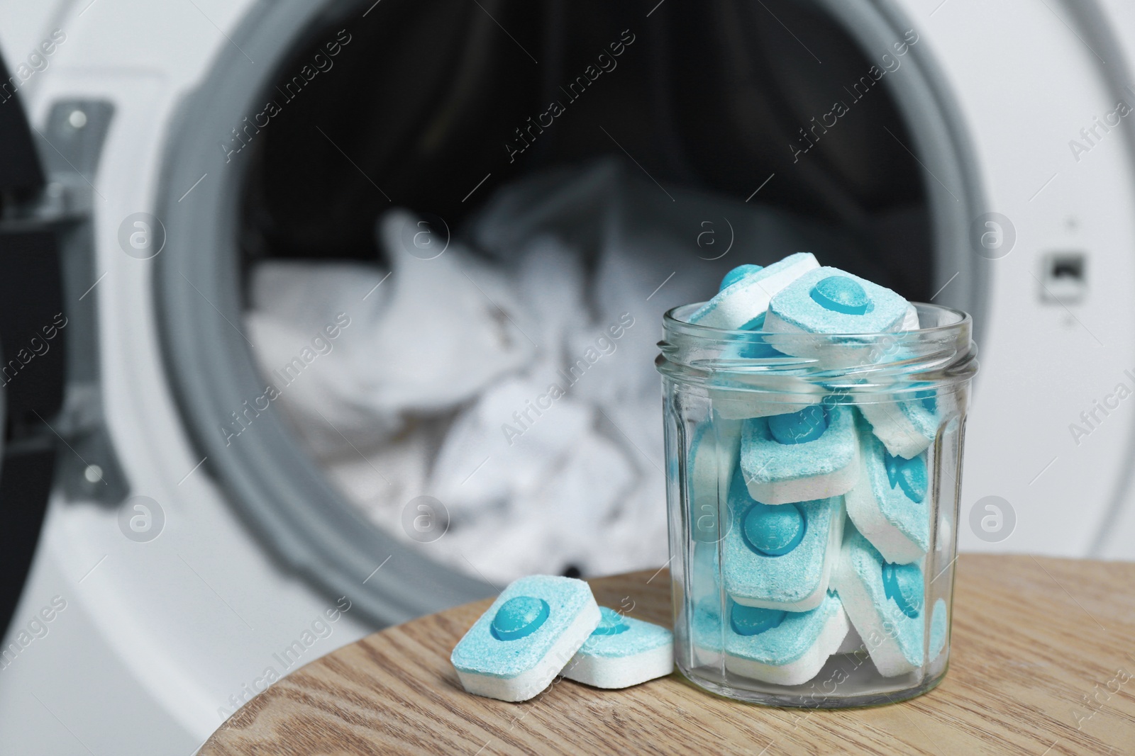 Photo of Jar with water softener tablets on wooden table near washing machine