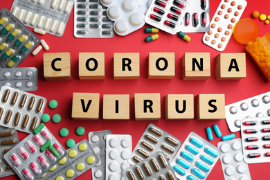 Photo of Wooden cubes with words CORONA VIRUS and medicine on red background, flat lay