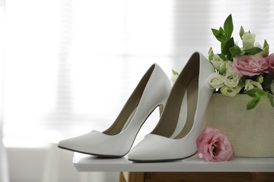 Photo of Pair of white high heel shoes and wedding bouquet on table indoors, space for text