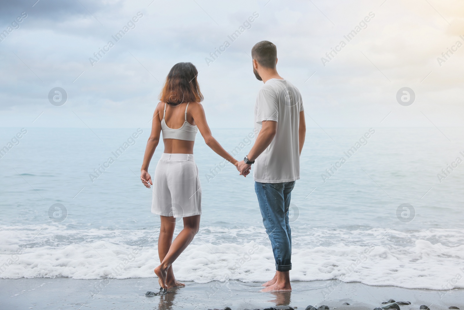 Photo of Young couple spending time together on beach near sea, back view