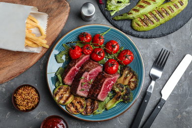Photo of Delicious sliced beef steak served on grey table, flat lay