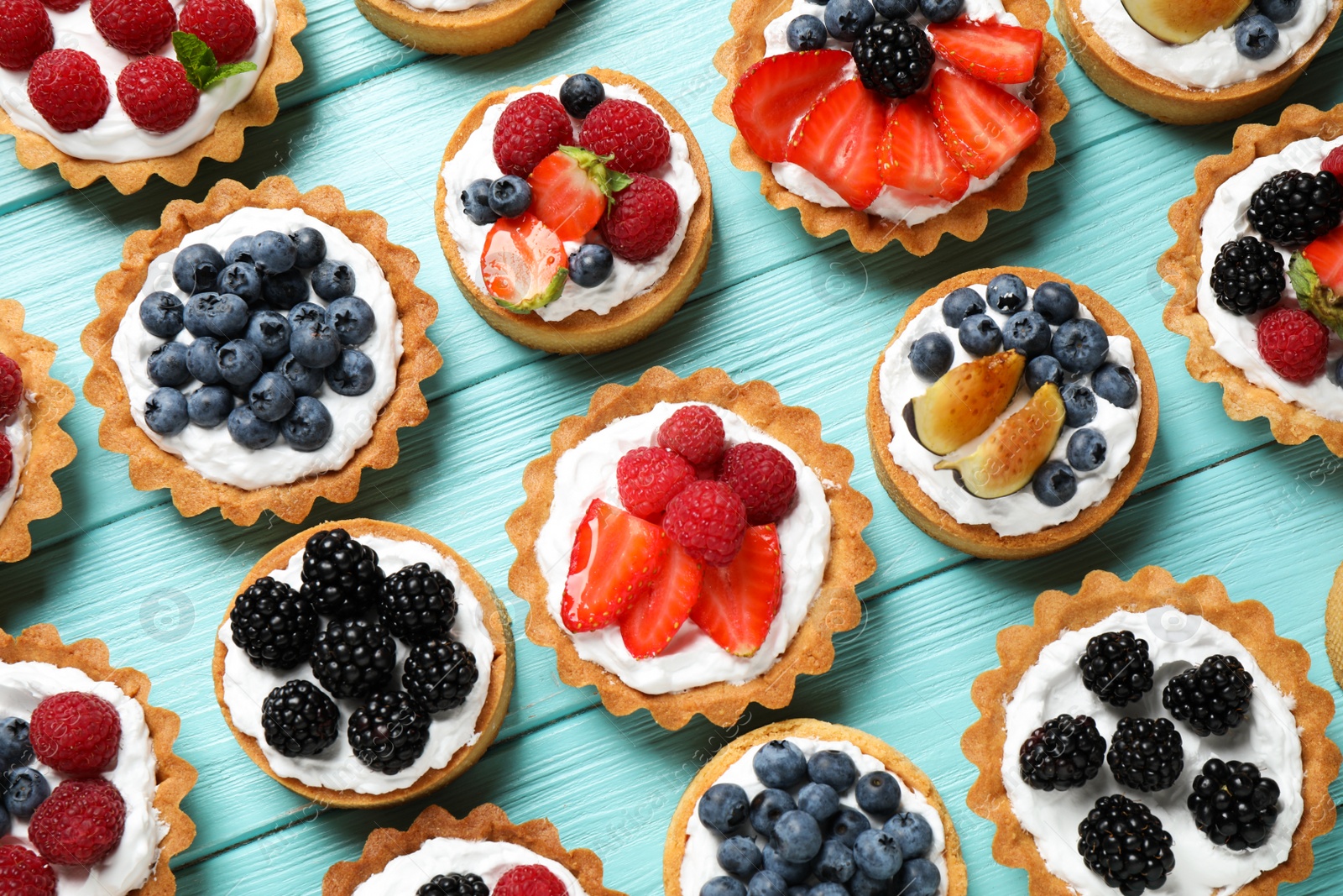 Photo of Many different berry tarts on blue wooden table, flat lay. Delicious pastries