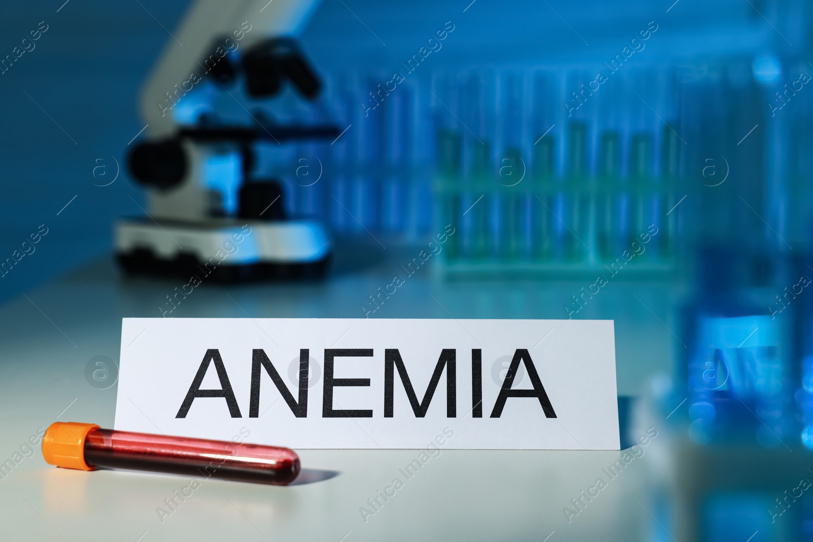 Photo of Test tube with blood sample and inscription Anemia on white table in laboratory. Space for text