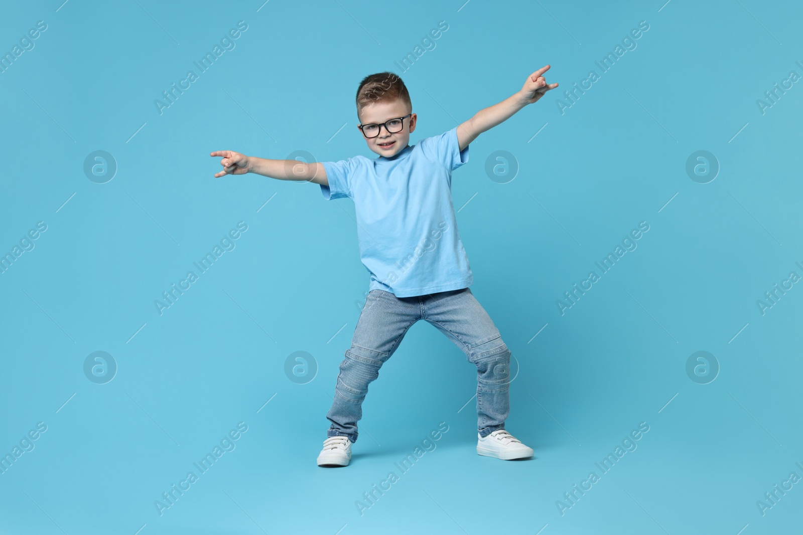 Photo of Happy little boy dancing on light blue background