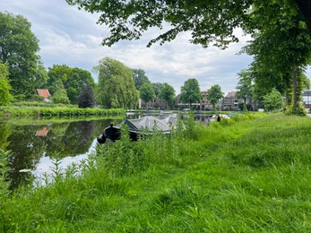 Photo of Beautiful view of city canal with moored boat surrounded by greenery