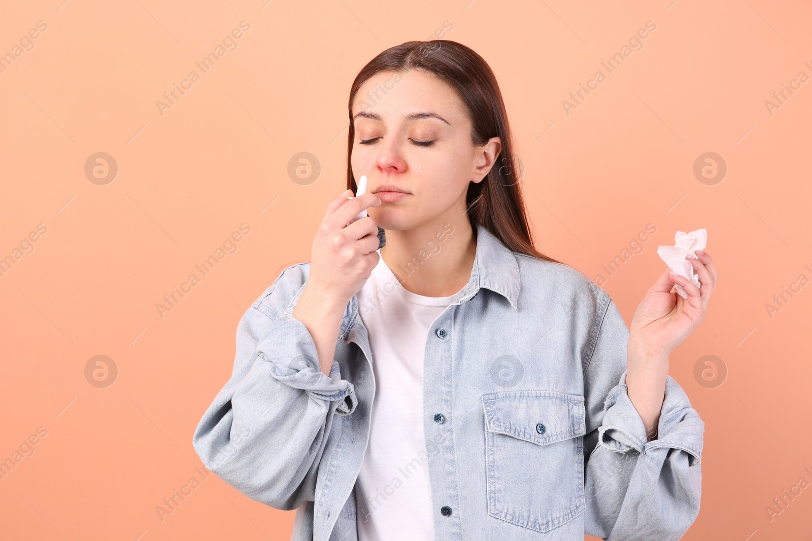 Photo of Woman using nasal spray on peach background