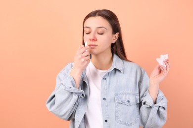 Woman using nasal spray on peach background