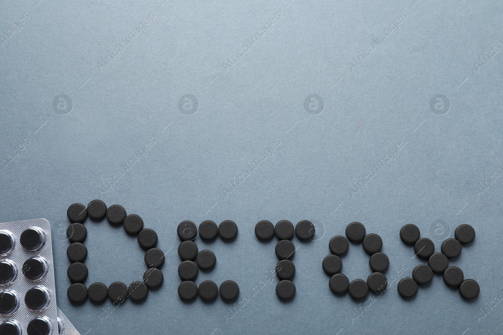 Photo of Word Detox made of activated charcoal pills near blisters on grey background, flat lay with space for text. Potent sorbent