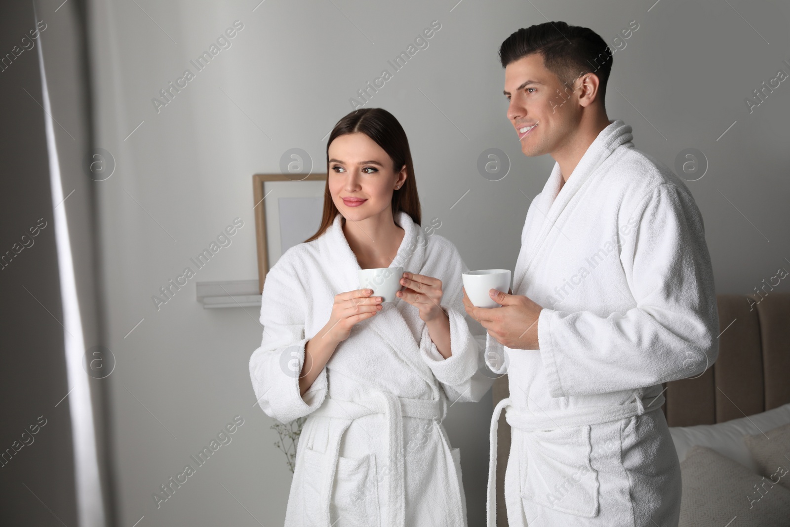 Photo of Happy couple wearing bathrobes near window in room
